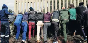  ?? /MDUDUZI NDZINGI ?? Thokoza residents break down a fence surroundin­g a field where the bodies of the two girls were found.