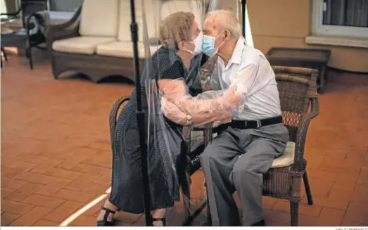 ?? EMILIO MORENATTI ?? Agustina Cañamero abraza y besa a su esposo Pascual Pérez a través de una pantalla plástica para evitar contraer el coronaviru­s en un asilo en Barcelona.