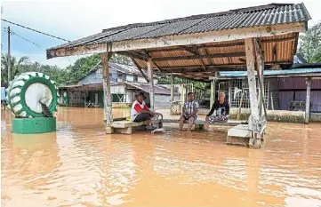  ?? — bernama ?? Water woes: (above) residents using a boat to evacuate a flooded area in Kampung Nibong. (Left) Three men watching the rising water level in Kampung Nibong.