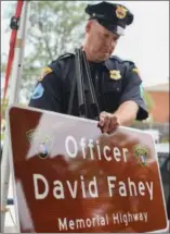  ?? ERIC BONZAR — THE MORNING JOURNAL ?? A Cleveland police officer holds on to a memorial highway plaque revealed in honor of fallen Officer David Fahey Jr. on July 10.