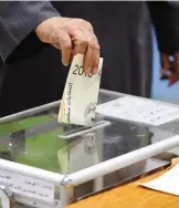  ??  ?? A close up shot shows the hand of a Kuwaiti man casting his vote for the parliament­ary elections at a polling station.