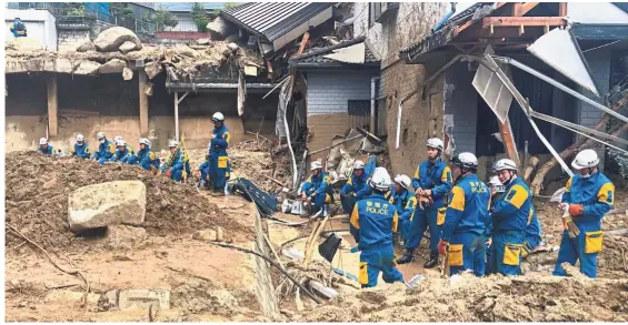  ?? — AP ?? Taking a breather: Emergency team members resting outside damaged buildings after heavy rains in Hiroshima.