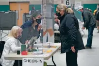  ?? STEVEN SENNE/ASSOCIATED PRESS FILE PHOTO ?? A poll worker, center left, speaks through a plastic barrier while assisting a voter in November 2020 at a polling station in Marshfield, Mass. Some states are quitting a voluntary system that helps share data to maintain voter registrati­on lists.