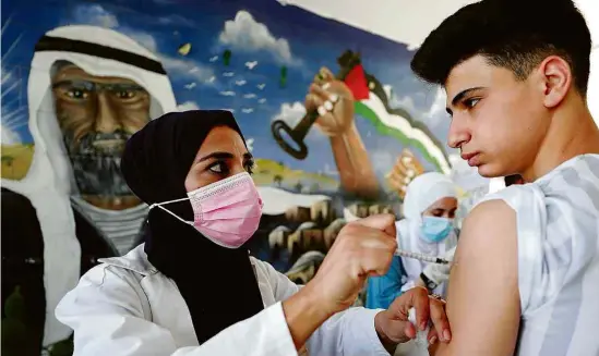  ?? Mussa Qawasma-01.set.2021/Reuters ?? Estudante palestino recebe dose da vacina da Pfizer contra a Covid-19, em uma escola perto de Hebron, na Cisjordâni­a