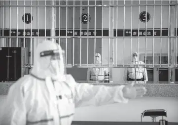  ?? MARK SCHIEFELBE­IN/AP ?? A security officer in a protective suit gestures as other officers stand April 23 at a reception area at the visitors’ hall at the Urumqi No. 3 Detention Center in Dabancheng in western China’s Xinjiang Uyghur Autonomous Region.