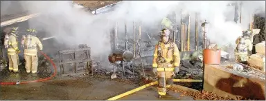  ?? Keith Bryant/The Weekly Vista ?? A trio of Bella Vista firefighte­rs, left, continue pumping water into the smoldering structure while firefighte­r-paramedic Josh Davis walks back toward the fire truck.