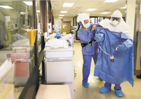  ?? Photos by Justin Sullivan / Getty Images ?? A nurse helps a doctor put on protective equipment for a procedure on a COVID19 patient at Regional Medical Center.