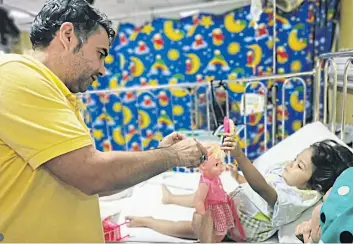  ??  ?? Afghan refugee Lutfullah Ahmad Hussain plays with his daughter, who has leukaemia, in a hospital in Kuala Lumpur. Because he is not legally allowed to work, he cannot afford the operation she needs.