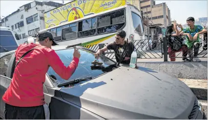  ?? EFE ?? Caracas. Jóvenes se dedican a limpiar vidrios de vehículos en un semáforo del centro de esta ciudad.