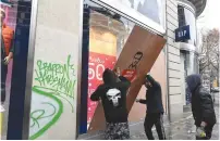  ?? (Piroschka van de Wouw/Reuters) ?? WORKMEN PLACE a wood panel to protect a broken window on a Paris store yesterday.