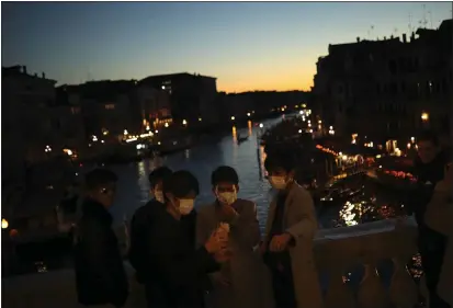  ?? FRANCISCO SECO — THE ASSOCIATED PRESS ?? Tourists wearing protective masks pose for a photograph at the Rialto bridge as the sun sets in Venice, Italy, Friday. Authoritie­s in Italy decided to re-open schools and museums in some of the areas less hard-hit by the coronaviru­s outbreak in the country which has the most cases outside of Asia, as Italians fear that the outbreak could plunge the country’s economy into recession.