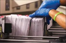  ?? JASON REDMOND/AFP/GETTY IMAGES ?? An election worker handles vote-by-mail ballots coming out of a sorting machine for the presidenti­al primary at King County Elections in Renton, Wash., on March 10.