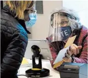  ?? STEVEN SENNE/AP ?? Poll worker Alice Machinist wears a mask and shield while assisting a voter last week in Newton, Massachuse­tts.