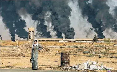  ??  ?? FIRE AND FURY: A Syrian woman stands before a backdrop of tire fires on Friday near the border town of Ras al-Ayn, which saw fighting that morning despite a US-backed cease-fire announced Thursday.