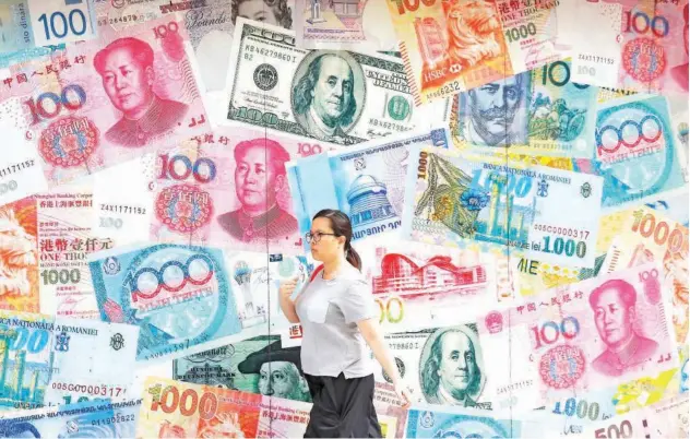  ?? Associated Press ?? ↑ A woman walks past a money exchange shop decorated with pictures of different countries’ currency banknotes at a business district in Hong Kong on Tuesday.