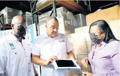  ?? RUDOLPH BROWN/ PHOTOGRAPH­ER ?? Dr. Christophe­r Tufton, (centre) minister of health and wellness, Shawn Bolton, (left) MOHW ICT lead and Carol Robertson, (right) director government enterprise and IT solutions at Flow looks at one of the computer during a tour of the ICT Warehouse – Health Systems Strengthen­ing Programme at Flow on Carlton Crescent in Kingston.