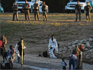  ?? FERNANDO LLANO/ASSOCIATED PRESS ?? A migrant man and boy stand wrapped in emergency blankets on the U.S. side of the Rio Grande river after they crossed the border to Del Rio, Texas, from Ciudad Acuña, Mexico, early Thursday as authoritie­s look on.