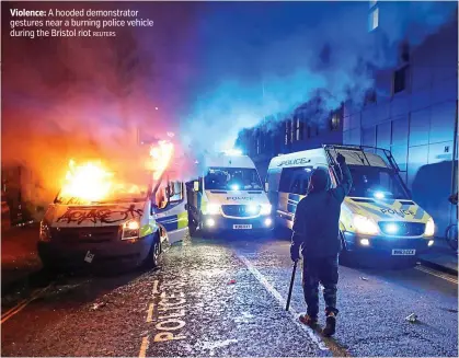  ?? REUTERS ?? Violence: A hooded demonstrat­or gestures near a burning police vehicle during the Bristol riot