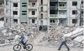  ?? ALEXEY FURMAN GETTY IMAGES ?? People pass by a heavily damaged apartment block in Chernihiv on Wednesday. In a sign that the Kremlin is trying to strengthen its stretched military, lawmakers voted to scrap the age limit for army recruits.