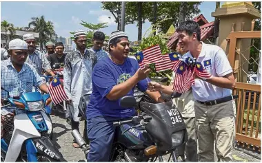  ?? — Bernama ?? Flags for the faithful: Tan (right) distributi­ng Jalur Gemilang while chatting with residents leaving Taming Jaya Mosque after Friday prayers.