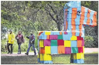  ?? RALPH BARRERA / AMERICAN-STATESMAN ?? Mike and Miki Kelly (left) and Joe Leggs walk by one of a herd of piñata burros created by David Goujon. Goujon created his art installati­on, “Las Piñatas,” in response to the bulldozing of a family’s piñata business. The Austin Art in Public Places...