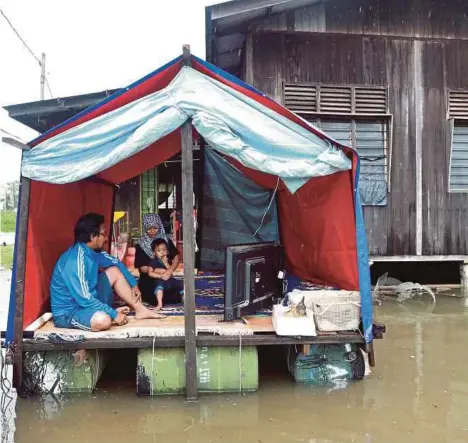  ?? PIC BY MUHD ASYRAF SAWAL ?? Hafizzuddi­n Kamaruddin and his wife Suraya Kassim and their son Mohamad Mirza Al-Riki seeking shelter in a floating shed built with 10 empty oil barrels outside their home in Kampung Bukit Rangin in Kuantan yesterday.