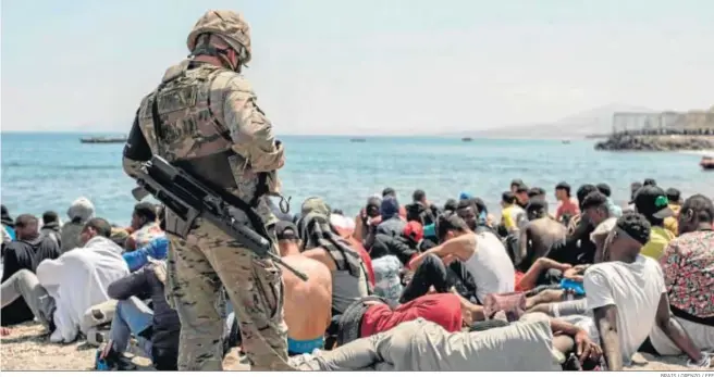  ?? BRAIS LORENZO / EFE ?? Un soldado del Ejército de Tierra junto a un grupo de inmigrante­s ayer en la playa fronteriza de El Tarajal de Ceuta.