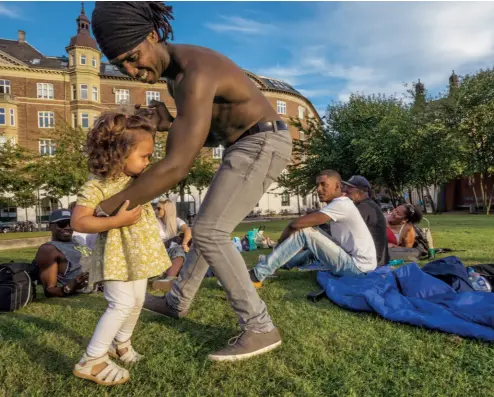  ?? CORY RICHARDS ?? Un imigrant cubanez adoptă pasiunea danezilor pentru socializar­e și dansează cu fiica lui, pe jumătate daneză, pe o peluză de lângă un ștrand – un loc de întâlnire popular din Copenhaga. Danezii sunt în continuare primitori cu imigranții, deși recenta...