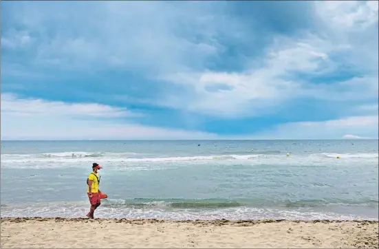  ?? MANÉ ESPINOSA ?? Un vigilant recorrent la platja de Castelldef­els un dia de juliol desagradab­le per al bany