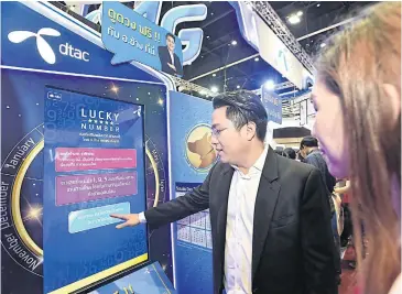  ??  ?? Famous fortune teller Tossaporn Sritula, widely known as Master Chang, demonstrat­es buying a SIM using DTAC’s Xiang Xiem luckynumbe­r SIM machine at Thailand Mobile Expo 2018.