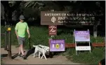  ?? JANE TYSKA — STAFF PHOTOGRAPH­ER ?? Michael Blake, of Oakland, walks his dog Dolly past social distancing warning signs at the Parkridge Gate in Anthony Chabot Regional Park in Oakland on Tuesday.