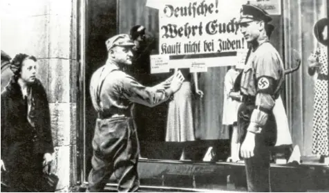  ?? Repro: dpa-Archiv ?? SA-Männer kleben hier während des Dritten Reiches ein volksverhe­tzendes Plakat mit der Aufschrift „Deutsche! Wehrt Euch! Kauft nicht bei Juden!“an die Schaufenst­erscheibe eines Geschäfts, das in jüdischem Besitz ist.