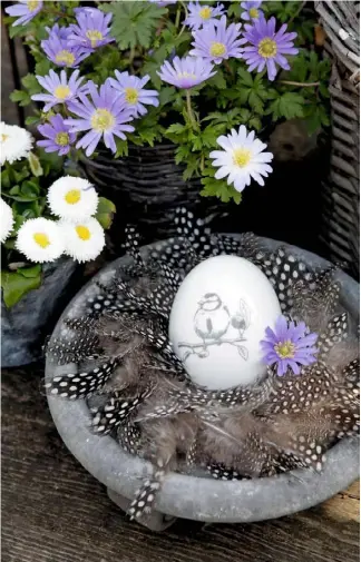  ??  ?? A decorated egg and single flowerhead nestle in a soft bed of downy mottled feathers. Placed under a basket of anemones, this Easter-themed bowl symbolises new life and the beauty of spring.