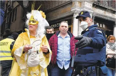  ?? LUIGI COSTANTINI AP ?? A police officer wearing a sanitary mask directs a Carnival participan­t in Venice on Sunday. The event is shutting down early.