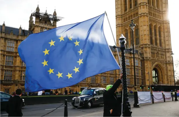  ?? (Reuters) ?? AN ANTI-BREXIT protester ties an EU flag to a lamp post yesterday outside the Houses of Parliament in London.