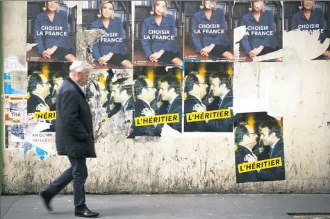 ??  ?? A man walking Friday in Paris passes vandalized campaign posters for the French presidenti­al election to be held Sunday.