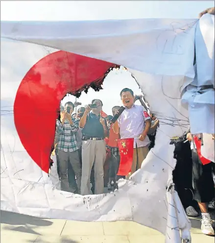  ?? REUTERS ?? Cuestión de símbolos. Unos manifestan­tes toman fotos y se ríen ante la bandera nacional japonesa quemada durante una protesta anti Japón en Wuhan, provincia de Hubei