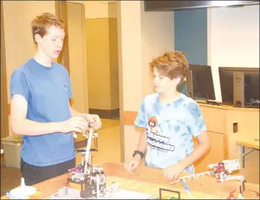  ?? (NWA Democrat-Gazette/Marc Hayot) ?? Paxton Weathers (left) explains to his brother Joshua how to attach a part on one of the robots at a practice session for the LEGO robotics team Happy Accidents on May 2. Happy Accidents recently competed in the LEGO Robotics First Championsh­ip in Houston.