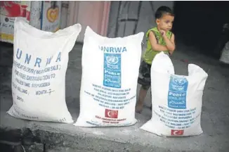  ??  ?? Un niño palestino pasa junto a unos sacos de alimentos facilitado­s por la UNRWA.