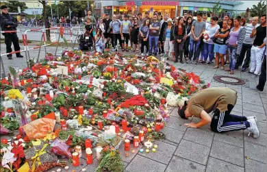  ?? ARND WIEGMANN / REUTERS ?? A man prays beside flowers laid in front of the Olympia shopping mall in Munich, Germany, where Friday's shooting rampage started.