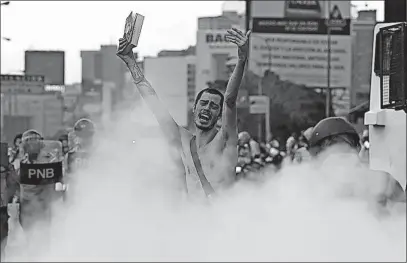  ?? [FERNANDO LLANO/THE ASSOCIATED PRESS] ?? An anti-government protester, wearing only sneakers and tube socks, holds a Bible in the middle of a cloud of tear gas during a march Thursday in Caracas, Venezuela. The man, whose back was marked with bruises from rubber bullets, approached heavily...