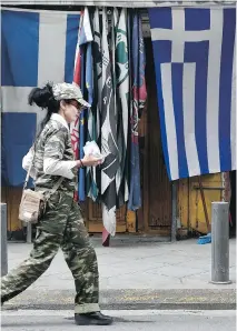  ??  PETROS GIANNAKOUR­IS/THE ASSOCIATED PRESS ?? A woman walks past a kiosk in central Athens on Thursday. Greece’s Prime Minister Alexis Tsipras sounded optimistic as he arrived at his first summit with European leaders.