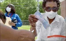  ??  ?? The Rev Eileen Smith hands out masks Friday in Arlington Heights.