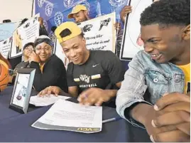  ?? KENNETH K. LAM/BALTIMORE SUN ?? Adrian Baldwin, center, of St. Frances Academy, signs his National Letter of Intent to play basketball at VCU. Watching are his mother, Nina, left, and older brother Jamaal.