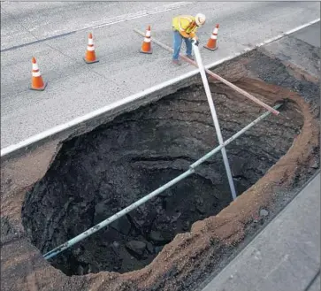  ?? Hayne Palmour I V San Diego Union- Tribune ?? A REPAIR WORKER places a pipe into a large sinkhole that opened on the right shoulder of Interstate 8 between College Avenue and Waring Road in San Diego. A Caltrans geologist will analyze the hole.