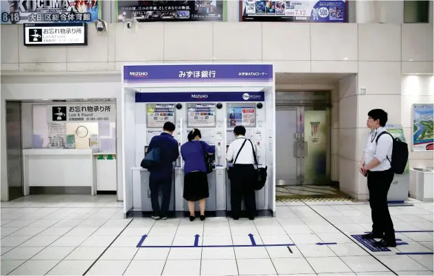  ?? Agence France-presse ?? ↑ Customers use a bank’s ATM in Tokyo.