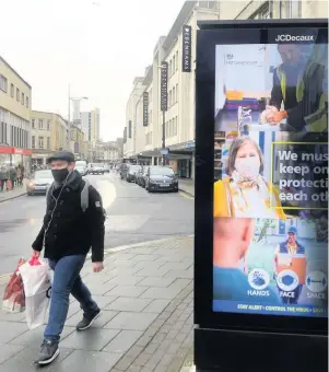  ??  ?? A shopper in Bristol walks past a coronaviru­s safety poster