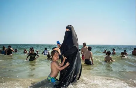  ?? DONATO DI CAMILLO PHOTOS ?? A woman wades on the shore, her young son tugging at her waist, part of the photograph­er’s Beach Body Bingo series.