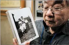  ?? AP ?? Les Ouchida holds a 1943 photo of himself and his siblings taken at an internment camp.