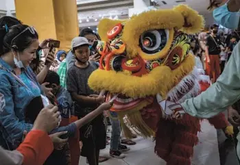  ?? ULET IFANSASTI/GETTY ?? A lion dancer accepts a donation from a boy on Saturday at a shopping center in Bogor, Indonesia, ahead of celebratio­ns marking the Lunar New Year. Lion dancers mimic the animal’s movements while performing, and it is believed that the dance wards off evil and brings good luck. The Lunar New Year — the Year of the Tiger — begins Feb. 1.